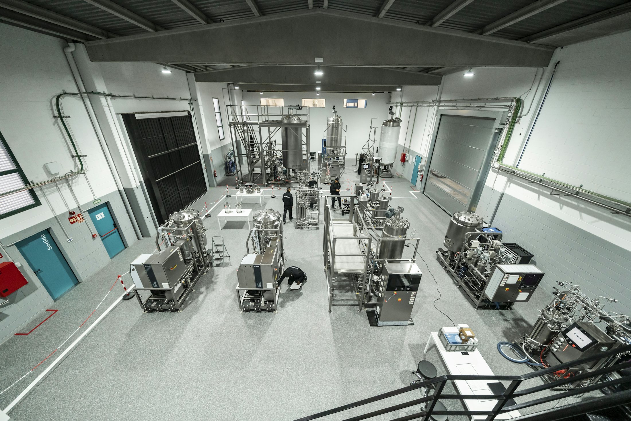 Large industrial bioprocess facility with stainless-steel vessels, piping and production skids